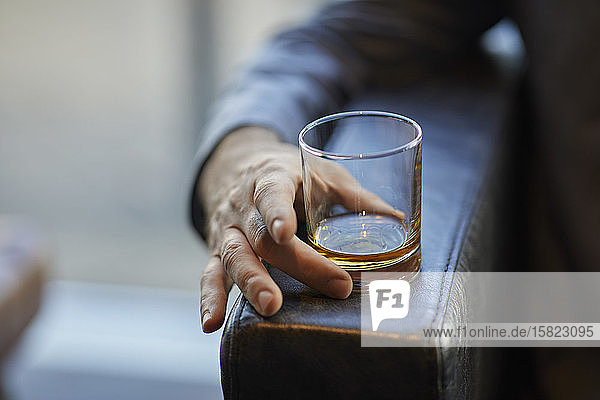 Nahaufnahme eines Mannes mit Whiskeyglas auf der Armlehne eines Lederstuhls