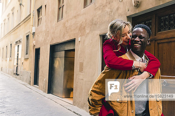 Glücklicher junger Mann trägt seine Freundin huckepack in einer Gasse in der Stadt Florenz  Italien