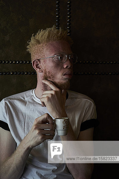 Albino man holding a cup of coffee and looking sideways