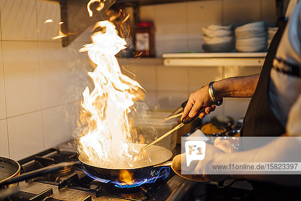 Indischer Koch beim Flambieren von Speisen in der Restaurantküche  Nahaufnahme