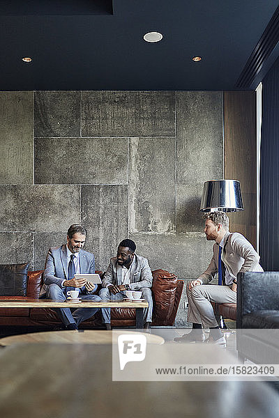 Three businessmen sitting in hotel lobby with tablet