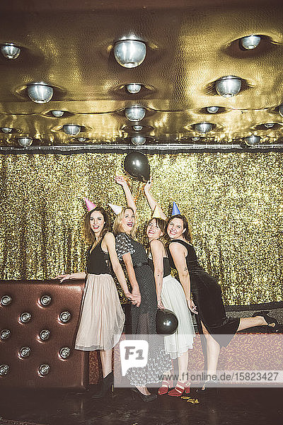 Porträt von vier glücklichen Frauen mit Partyhüten in einem Club