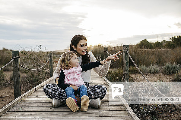 Happy mother and daughter sitting on a boardwalk in the countryside