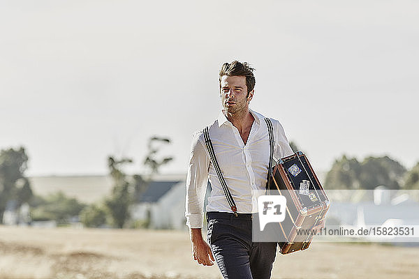 Man in old-fashioned clothes with suitcase in the countryside