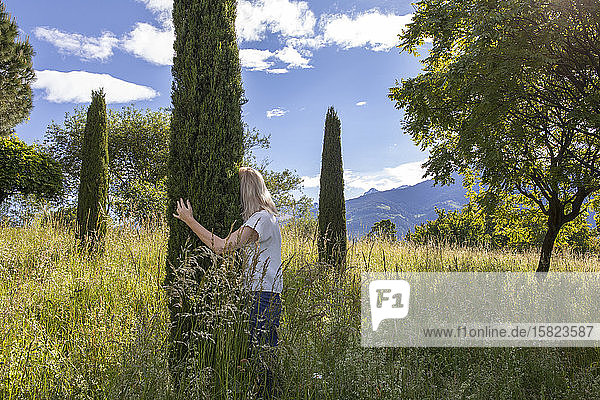 Woman standing in meadow hugging cypresse