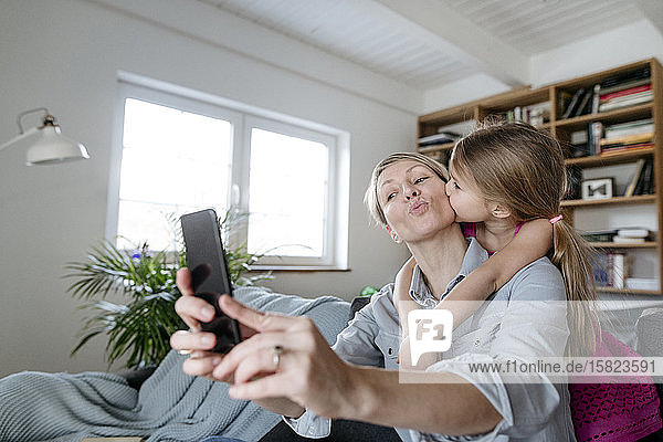 Mutter und kleine Tochter nehmen sich mit dem Smartphone zu Hause ein
