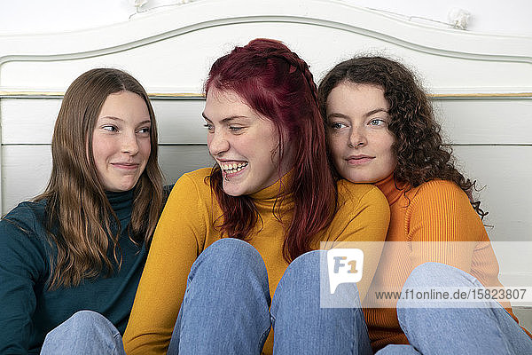 Portrait of three happy sisters sitting together on bed