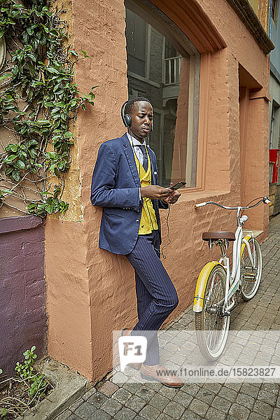 Stilvoller junger Geschäftsmann mit Fahrrad im altmodischen Anzug  der über Kopfhörer Musik hört