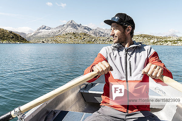 Junger lächelnder Mann in einem Ruderboot  Suretta-See  Graubünden  Schweiz