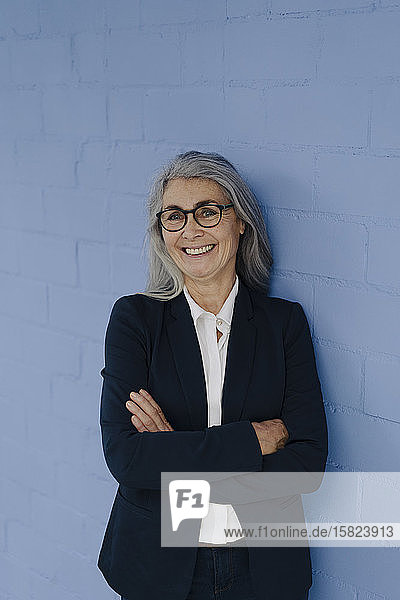 Porträt einer lächelnden grauhaarigen Geschäftsfrau  die an einer blauen Wand steht