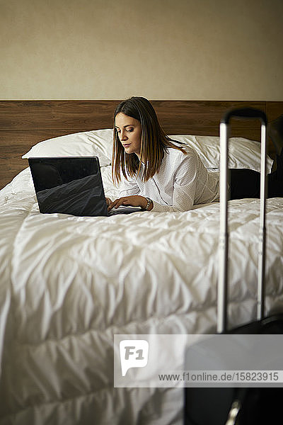 Geschäftsfrau  die im Hotelzimmer auf dem Bett liegt und einen Laptop benutzt