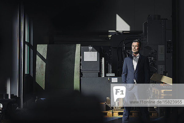 Businessman with closed eyes standing in a factory