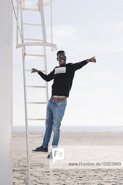 Stilvoller junger Mann steht am Strand auf einer Leiter
