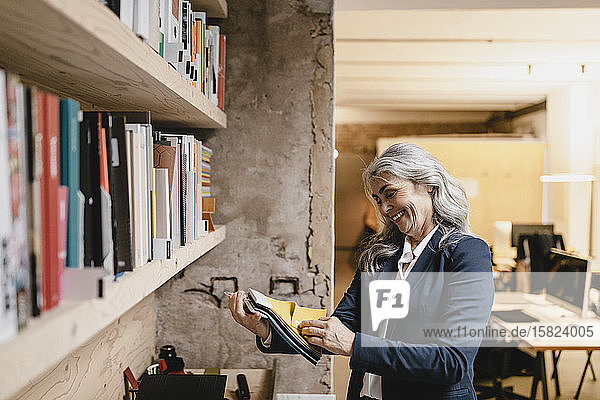 Lächelnde grauhaarige Geschäftsfrau hält Farbmuster in einem Loft-Büro