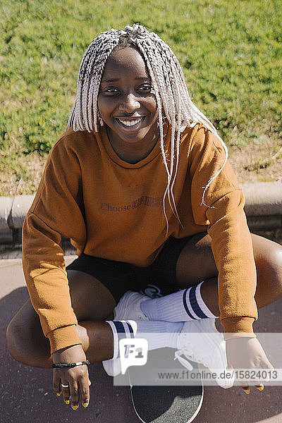 Porträt eines lächelnden Teenagers  der auf einem Skateboard sitzt
