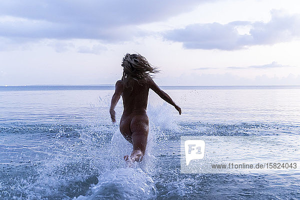 Rückenansicht einer jungen Frau  die bei Sonnenuntergang ins Meer läuft