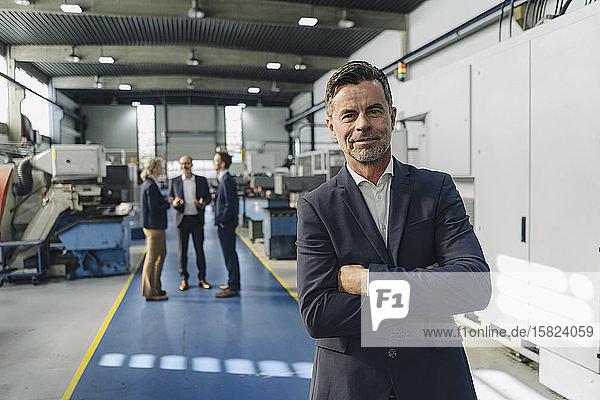 Porträt eines selbstbewussten Geschäftsmannes in einer Fabrik mit Kollegen im Hintergrund
