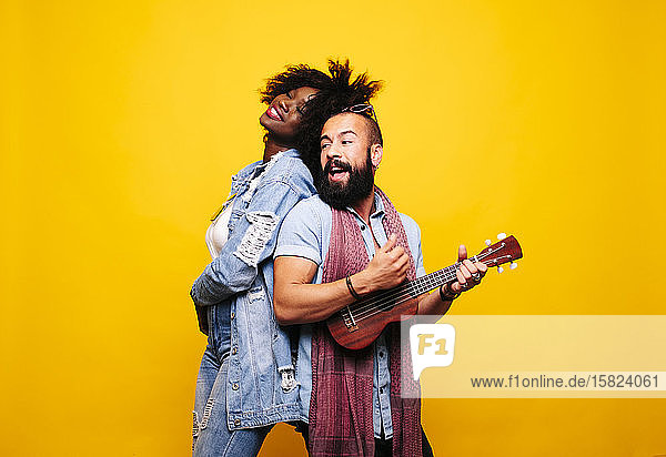 Glücklicher junger Mann mit Frau im Studio beim Ukulele spielen