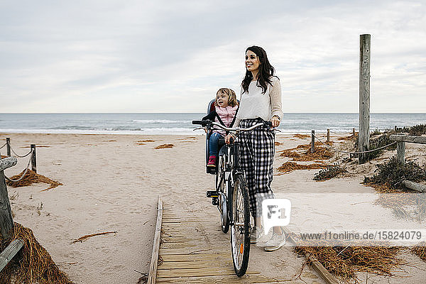 Woman with bicycle on a boardwalk in the dunes with daughter in child's seat