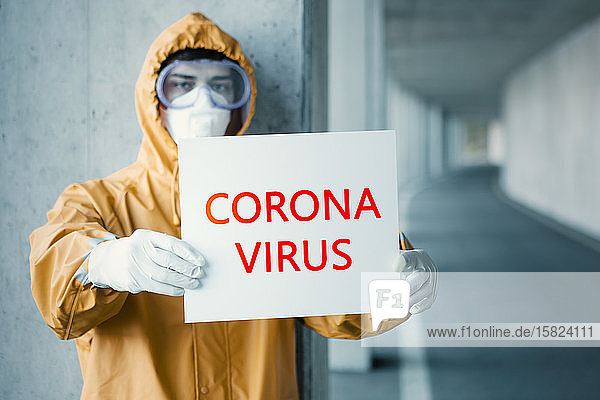 Porträt eines Mannes in Schutzkleidung mit Corona-Virus -Schild