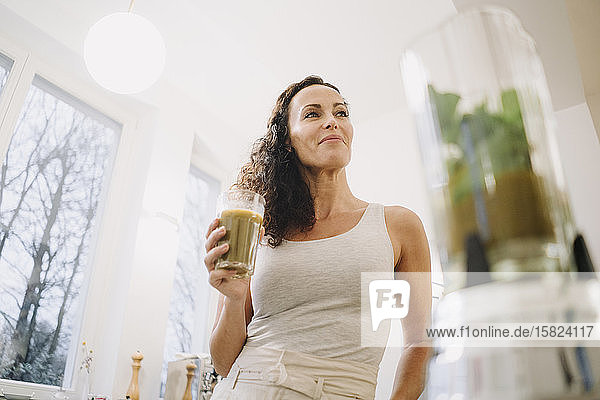 Fit woman standing in kitchen  drinking healthy smoothie