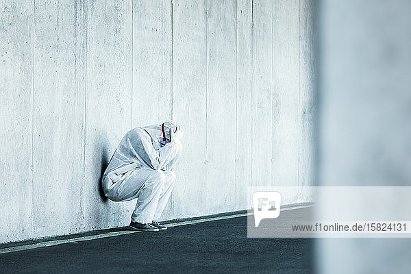 Verzweifelter Mann in Schutzkleidung lehnt an Betonwand