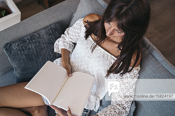 Junge Frau  die zu Hause auf der Couch sitzt und ein Buch liest