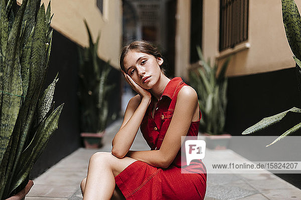 Portrait of female teenager wearing red strap dress in front of a wall