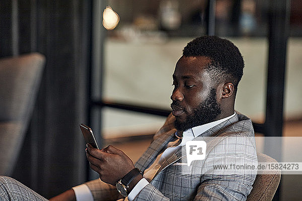 Businessman sitting in armchair using smartphone