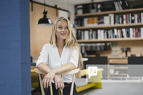 Portrait of a smiling young businesswoman sitting on a chair in loft office