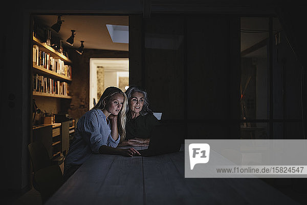 Mother and adult daughter looking at laptop on table in the dark