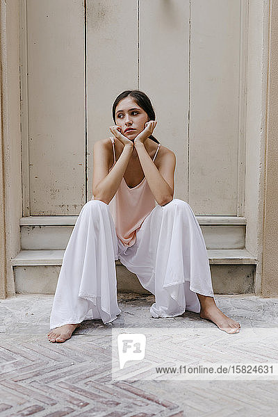 Porträt eines melancholischen Teenagers mit weißen Hosenröcken  der barfuß auf Stufen im Freien sitzt