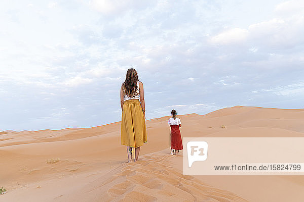 Rückansicht von zwei jungen Frauen auf einer Sanddüne in der Wüste Sahara Merzouga Marokko
