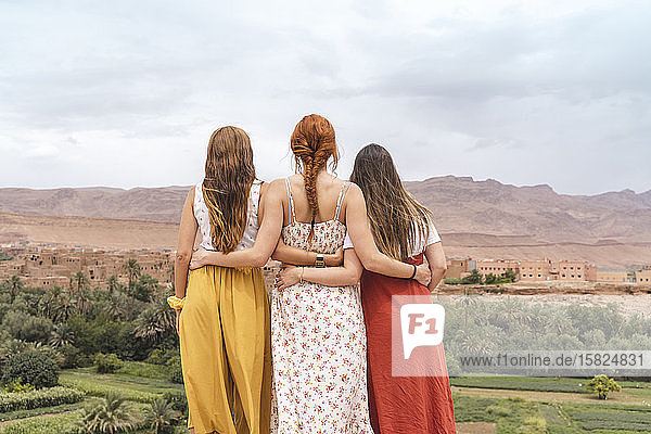 Rückenansicht von drei jungen Frauen  die Arm in Arm stehen und auf die Stadt blicken  Ouarzazate  Marokko
