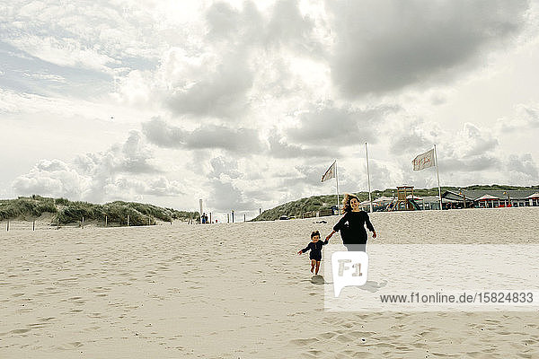 Mother and little daughter running hand in hand on the beach  The Hague  Netherlands