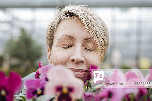 Smiling woman smelling on pansies in flower shop