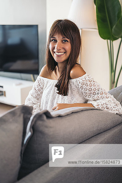 Portrait of smiling young woman sitting on the couch at home