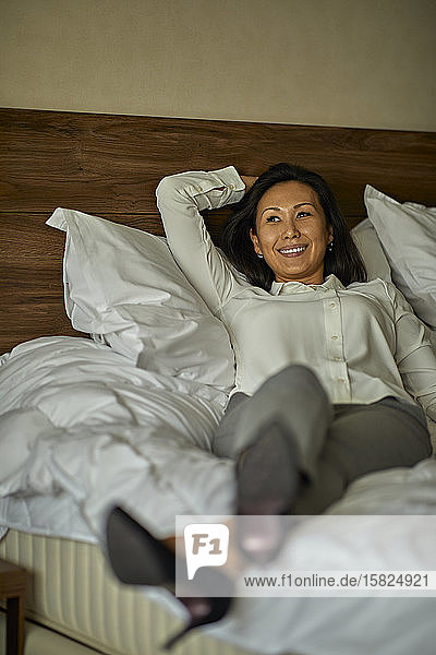 Smiling businesswoman lying on bed in hotel room