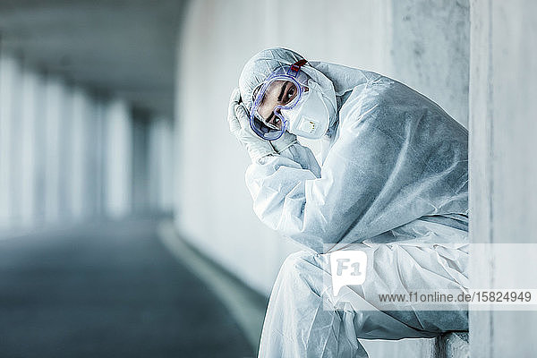 Bildnis eines Mannes in Schutzkleidung der in einer Nische einer Betonwand in einem Tunnel sitzt