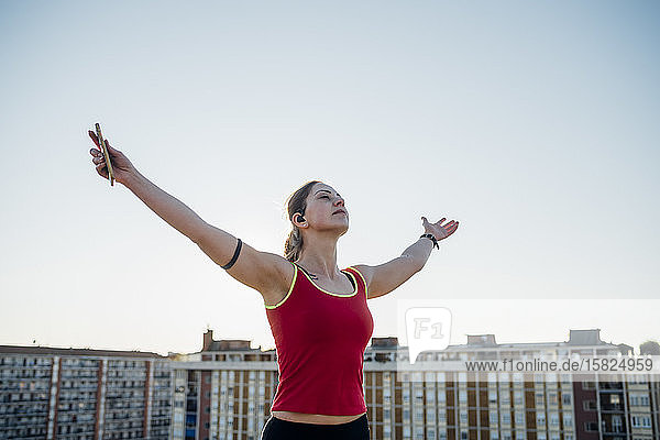 Sportliche junge Frau hebt ihre Arme unter blauem Himmel