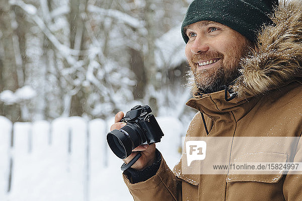Porträt eines glücklichen Mannes mit Digitalkamera im Winter