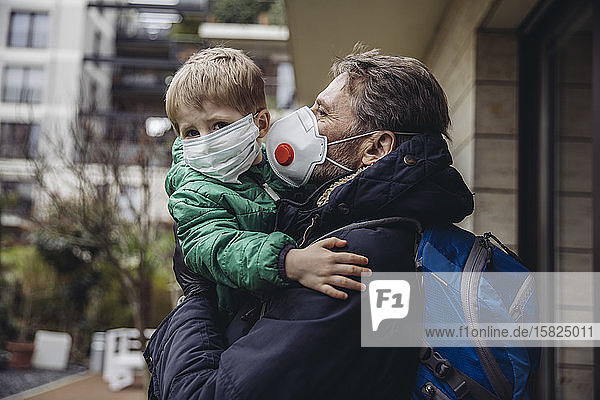 Vater trägt Sohn, beide tragen Schutzmasken, im Freien