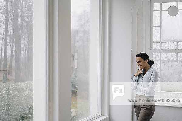 Successful businesswoman  looking out of window  holding smartphone