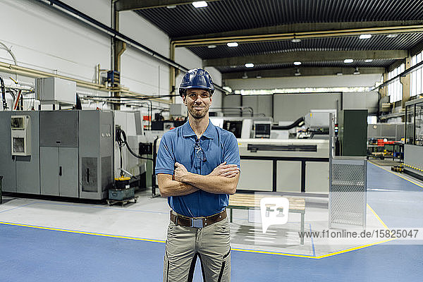 Porträt eines selbstbewussten Arbeiters in einer Fabrik mit Schutzhelm