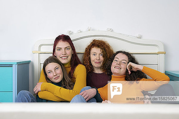 Portrait of mother and her three daughters sitting together on bed