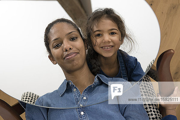Mirror image of smiling mother and her happy little daughter