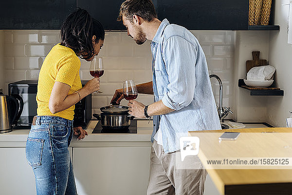 Junges Paar kocht und trinkt zu Hause gemeinsam Wein in der Küche