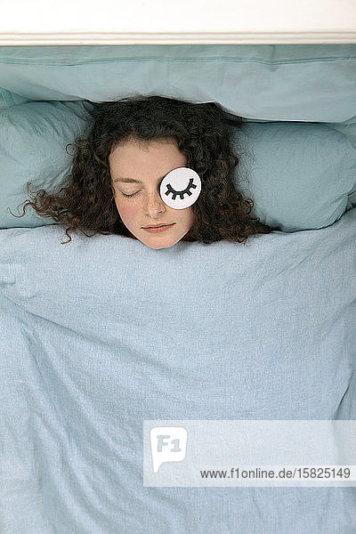 Portrait of sleeping young woman lying in bed with paper mask
