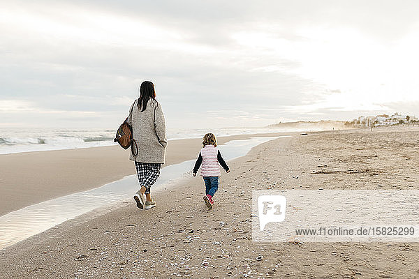 Rear view of mother and daughter walking on the beach at sunset