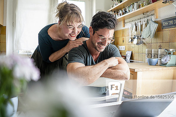 Happy couple in kitchen looking at laptop